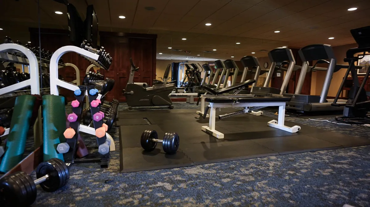 A bright, well-equipped fitness center featuring a range of equipment including dumbbells, a weight bench, treadmills, and other exercise machines. The space is open and motivating, inviting guests to engage in cardio workouts, weight training, or group fitness classes with a social vibe.