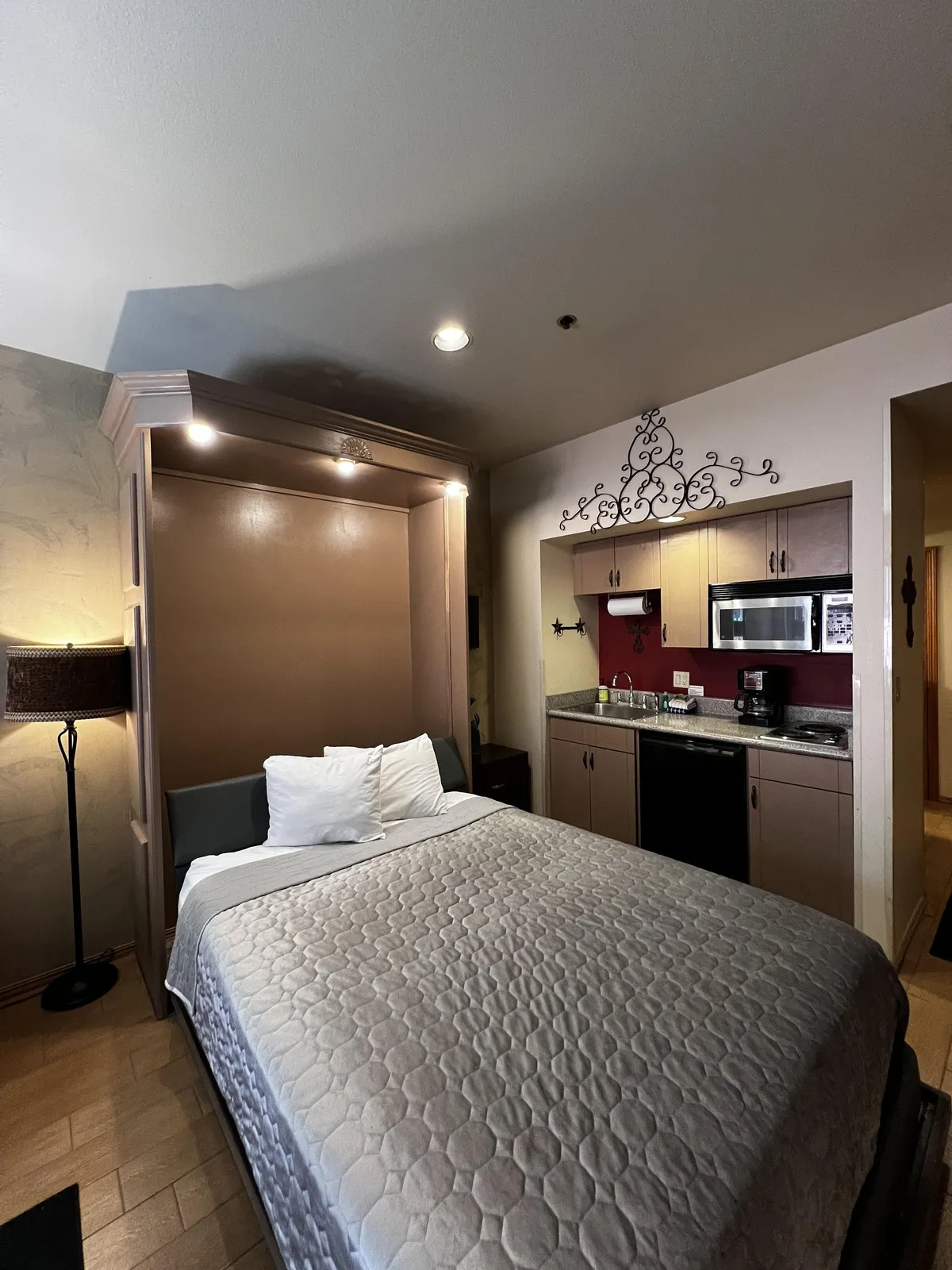 A cozy, homey interior showcasing the bed, kitchenette, a glowing lamp, and decorative wall piece. The image captures the lived-in feel of the space, suggesting cozy nights in, home-cooked meals, and relaxed mornings with coffee—all set against a charming mountain retreat backdrop.